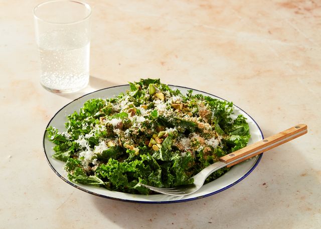 kale salad topped with cheese and pistachios in a white bowl with a blue rim on a marble background