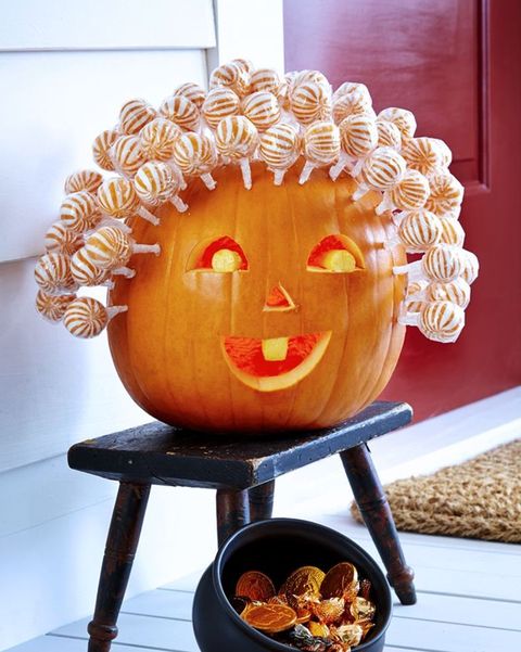 pumpkin carved with traditional jackolantern face, with spherical striped lollipops covering top to resemble hair
