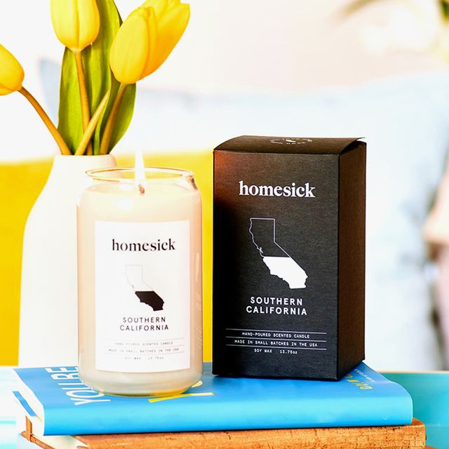 homesick candles sitting on stack of books in bright living room with yellow tulips and teal decor