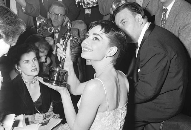 audrey hepburn, surrounded by photographers and reporters, holds up the academy award she won for best actress in roman holiday, her first american film