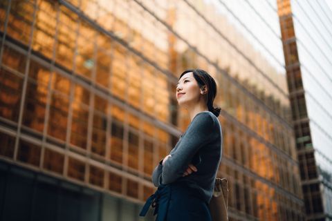 low angle portrait of confident and successful young asian businesswoman standing against contemporary corporate skyscrapers in financial district female leadership and determined to success