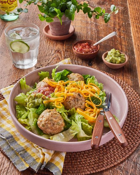 low carb tex mex chicken meatballs served over a bowl of lettuce with shredded cheddar and salsa in a pink ceramic bowl with a knife and fork
