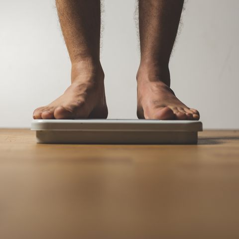 Low Section Of Man Standing On Weight Scale Over Hardwood Floor At Home