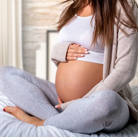Low Section Of Pregnant Woman Touching Belly While Sitting On Bed
