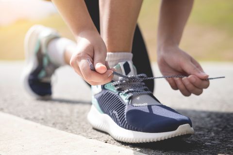 Low Section Of Woman Tying Shoelace On Road