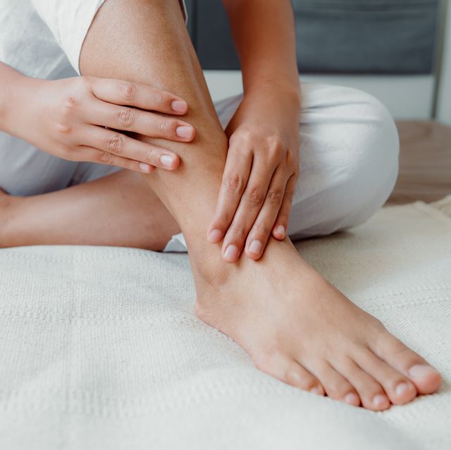 low section of woman with ankle pain sitting on bed