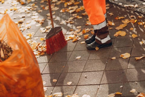 low section of worker sweeping footpath during autumn