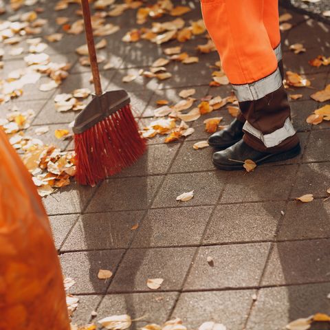 low section of worker sweeping footpath during autumn