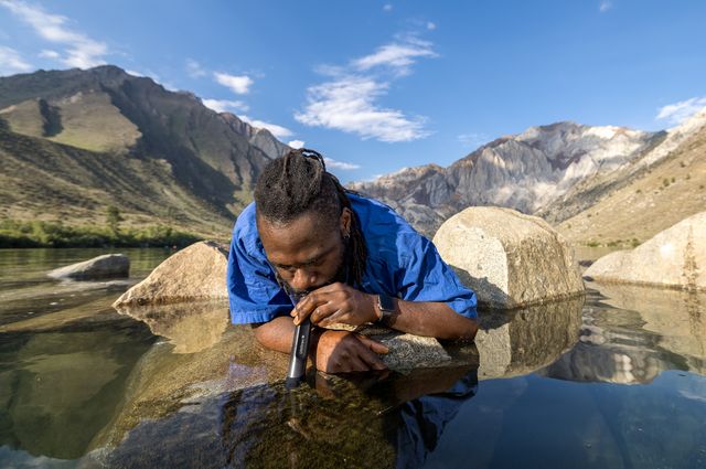 man drinking out of lifestraw from lake