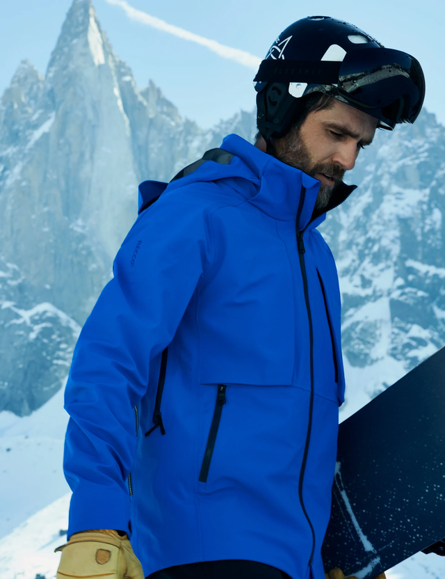 person in rain jacket on mountain carrying snowboard