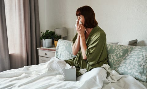 woman sneezing in bed with tissues