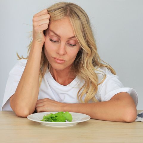 i'm fed up with untasty disgusting salad close up unhappy grimacing sad upset lady looking down at plate of lettuce on table