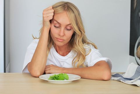 i'm fed up with untasty disgusting salad close up unhappy grimacing sad upset lady looking down at plate of lettuce on table