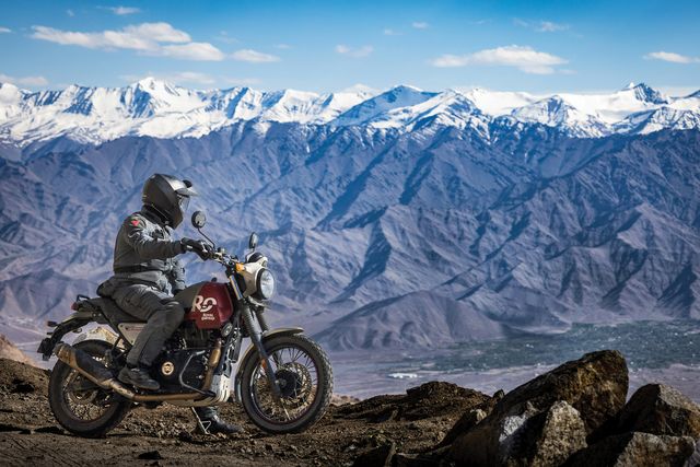 a man on a motorcycle overlooking snowy mountains