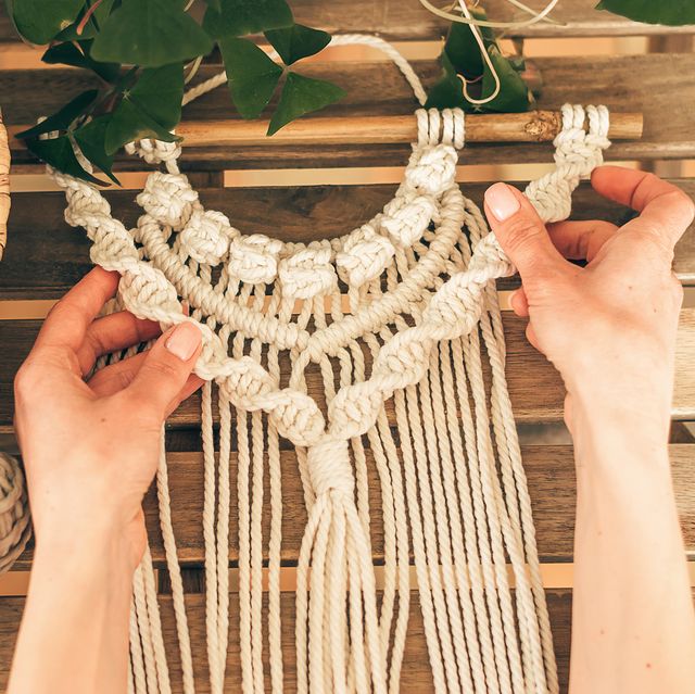 close up of women's hands weaving macrame from white cotton threads in a home workshophome decorhandmade conceptselective focus with shallow depth of field,top view