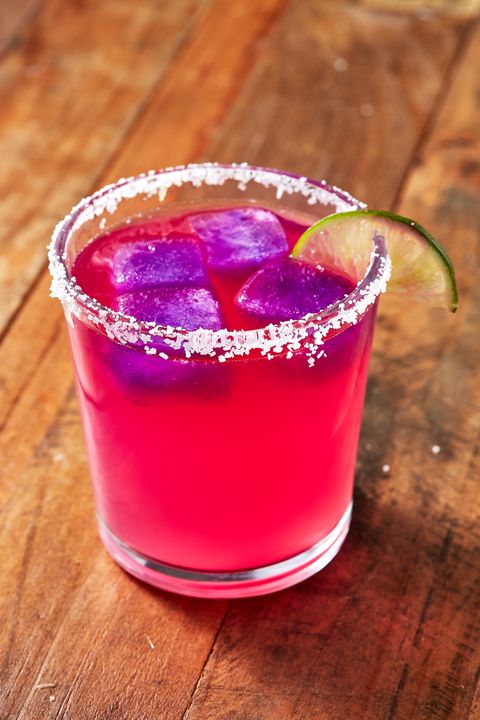 hot pink and purple margarita garnished with a lime and a salt rim on a wooden surface