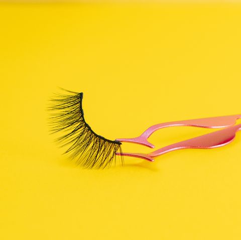 magnetic fake artificial eyelash in tweezers on yellow illuminating color background