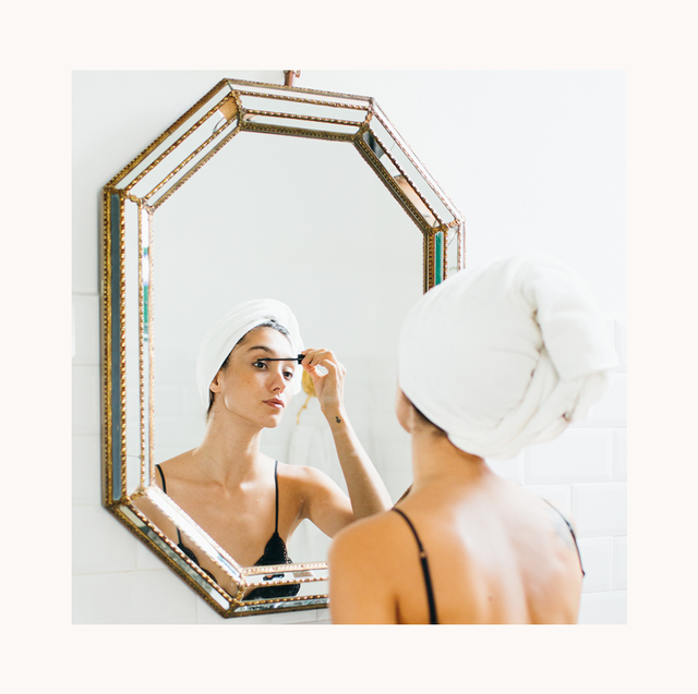woman with a towel over her head applying mascara in the mirror