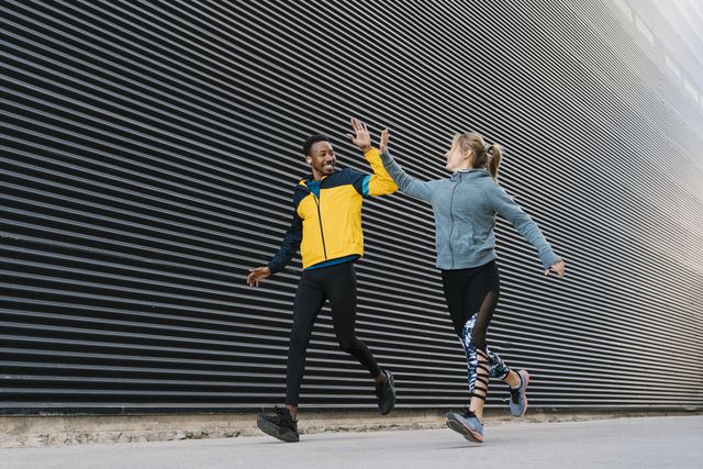 male and female sportsperson doing high
five while running on sidewalk during sports training by wall