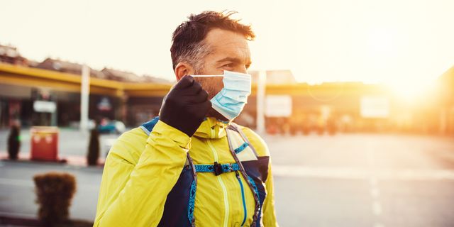 male jogger putting protective mask on his face to protect himself from virus or allergy infection sunset in the background