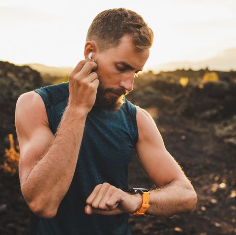 Male runner synchronizing wireless earphones with smart watch. Preparing for trail running outdoors at sunrise.