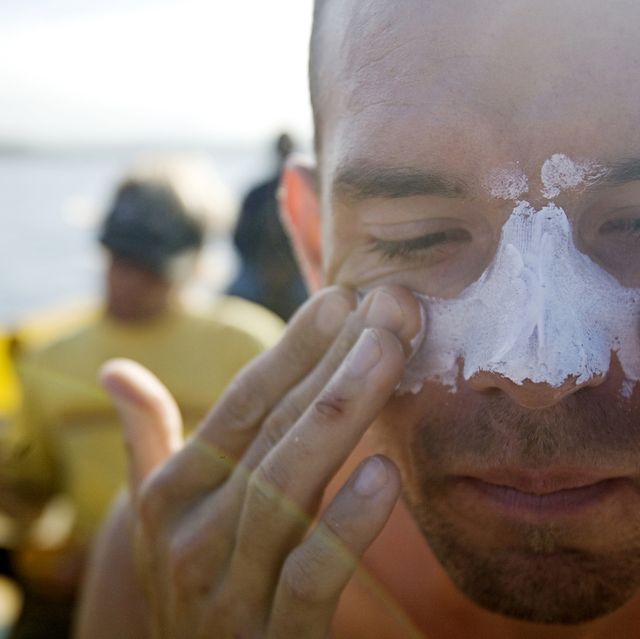 Man applies white zinc to his face and nose while sitting on a boat.