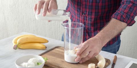 Man cooking tasty and healthy milkshake with banana and ice cream in home kitchen