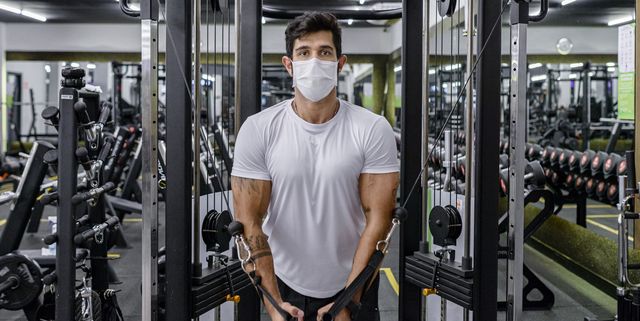 man doing strength training exercise in gym with face mask
