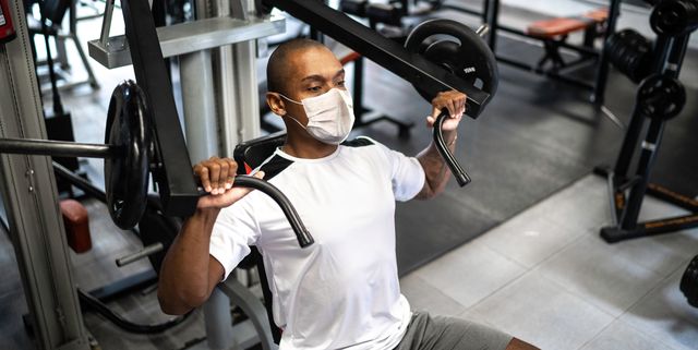 man doing strength workout exercise in gym with face mask