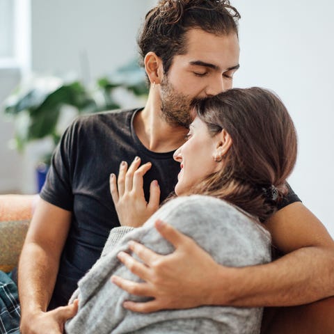 Man embracing girlfriend while kissing on her forehead at home