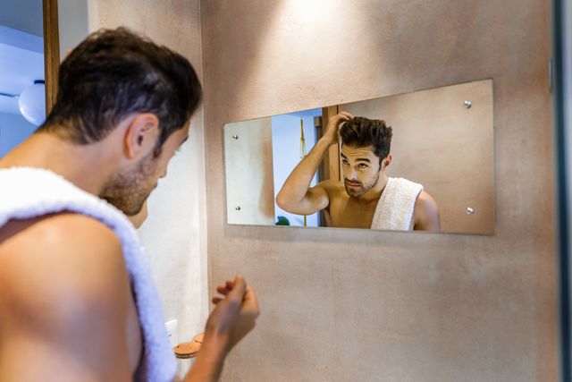man examining hair in mirror at bathroom at home