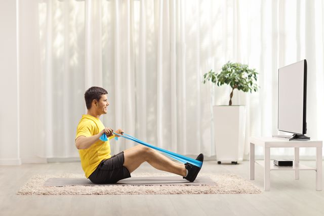 man exercising with an elastic band in front of a tv at home