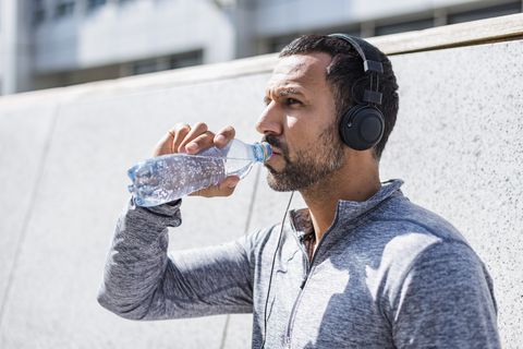 Man having a break from exercising wearing headphones and drinking from bottle