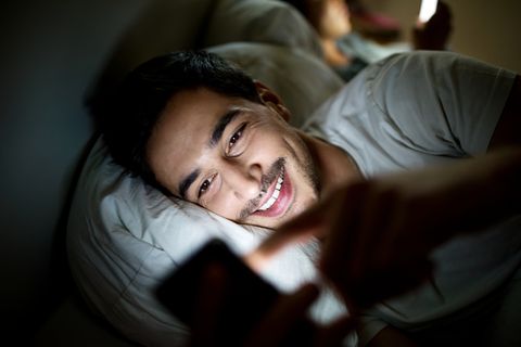 איש במיטה בודק את סטטוס המדיה החברתית שלו בסמארטפון