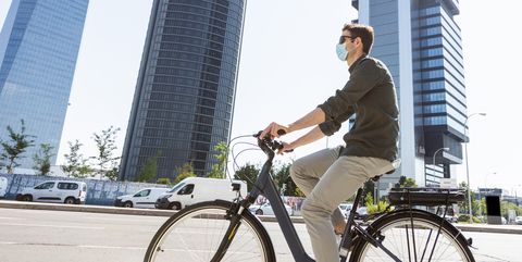 man in mask riding bicycle along street in city center