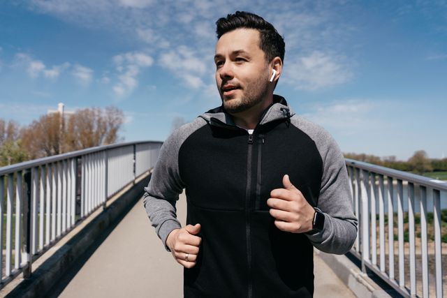 man jogging over a bridge wearing wireless in ear headphones
