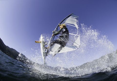 Man jumping wave on windsurf board, low angle view