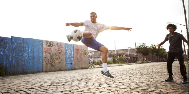 man kicking soccer ball while friend looking at street