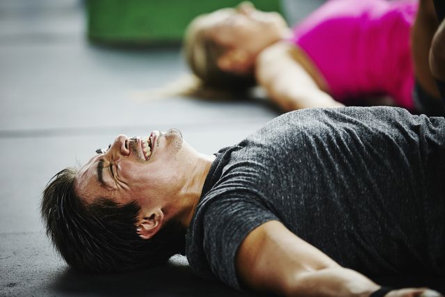 man laughing and grimacing lying on floor of gym