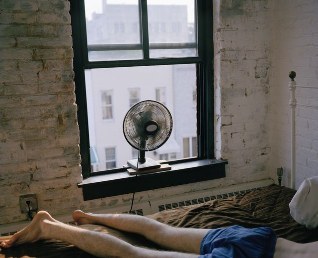 a man lying on a bed with a fan blowing