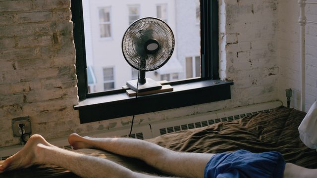 a man lying on a bed with a fan blowing