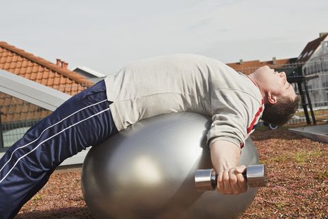 Man lying on fitness ball and holding dumbbells
