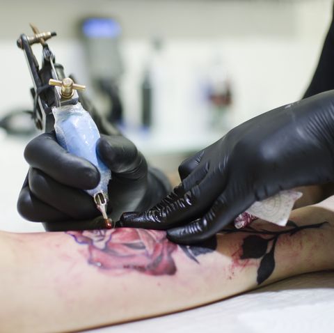 man making tattoo with equipment on woman hand