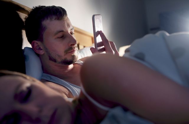 man on his phone in bed next to sleeping partner