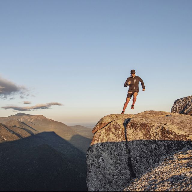 man runs along edge of cliff on top of mountain at sunset in maine