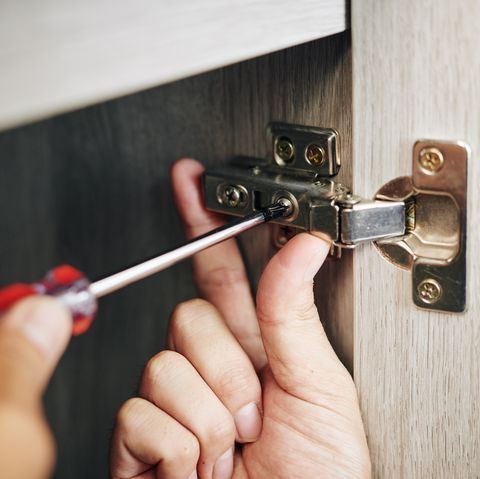 close up image of handyman assembling kitchen cabinet and screwing door hinge