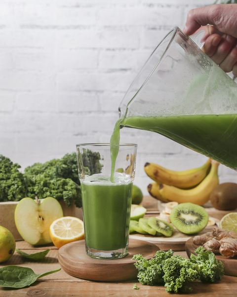 Man serving glass of green smoothie surrounded by ingredients