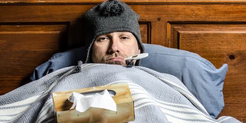 man sick in bed with a thermometer in his mouth