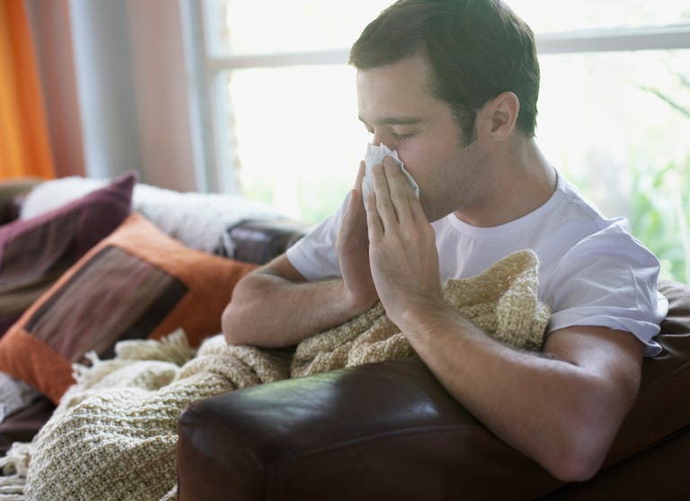 Man sitting in living room blowing nose