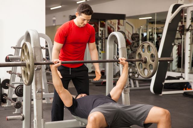 man spotting his friend on a bench press